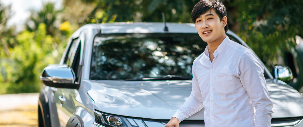 an asian man in white shirt standing next to his car